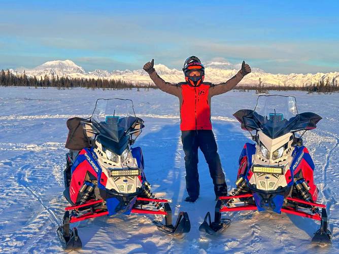Kim Bergeron stands with the two Polaris 600 cross-country snowmobiles they will be riding in the race.